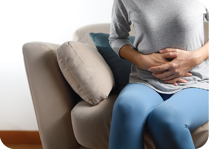 Eine Frau sitzt auf dem Sofa und fasst sich mit beiden Händen an den Bauch