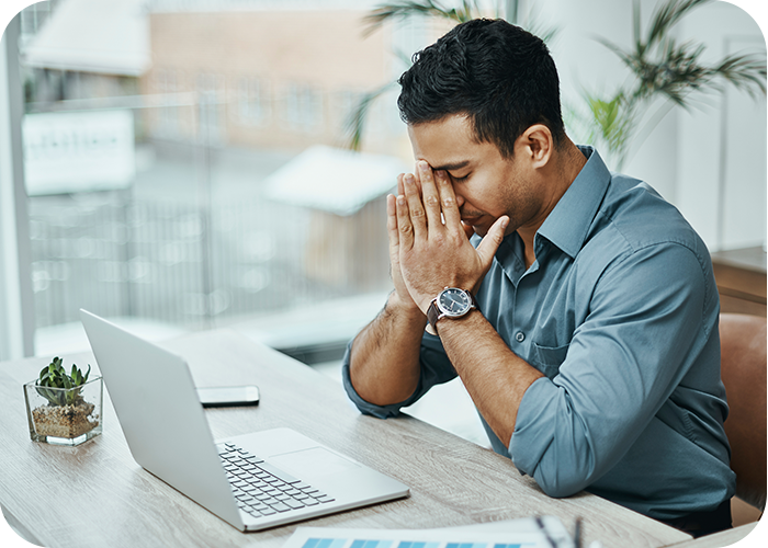 Ein Mann sitzt vor seinem Laptop und hat den Kopf in die Hände gestützt,